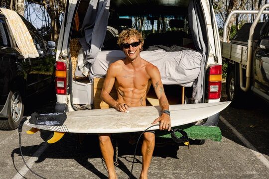 Man waxing surfboard at back of camper van in Australia