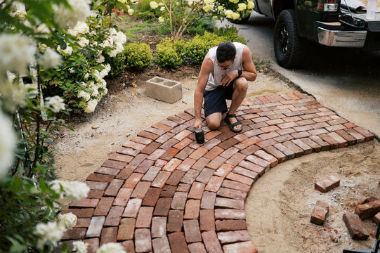 man using rubber mallet to secure bricks of a small walkway to house