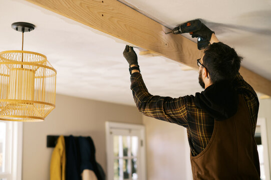 man wrapping old beam with white oak slabs inside his home