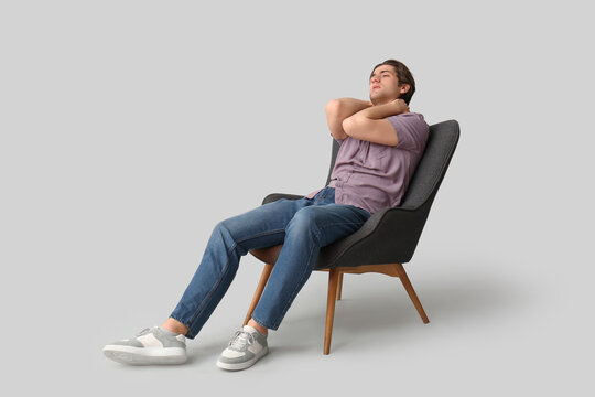 Weary young man sitting in armchair on light background