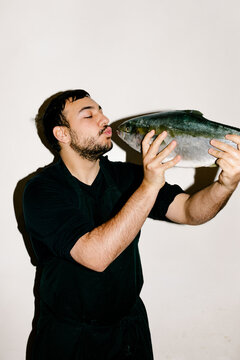 Chef with eyes closed and lips pursed leaning in toward a fresh fish