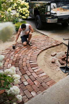 man using rubber mallet to secure bricks of a small walkway to house