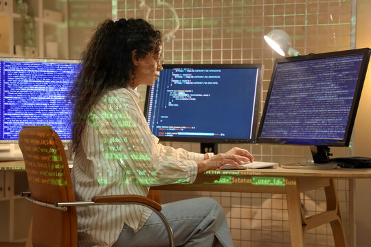 Female African-American programmer with computer monitors working in office at night
