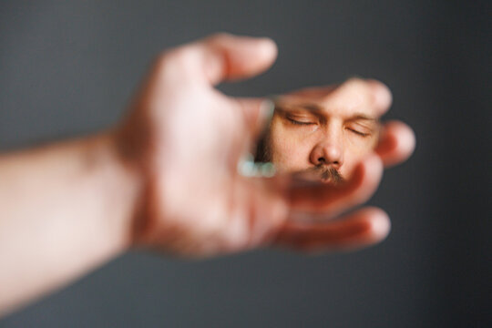 Man With Mirror Shows Face and Closed Eyes in Simple Setting