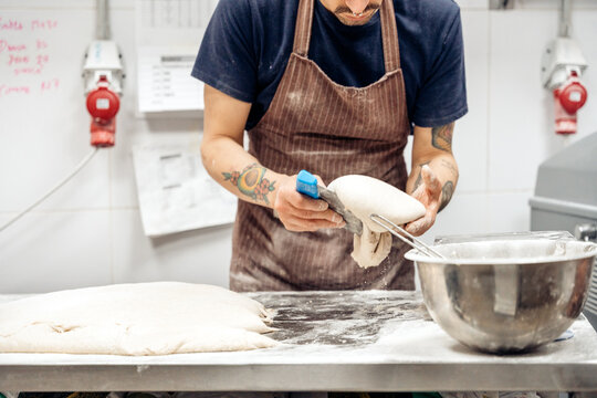 Baker portioning fresh dough in bakery kitchen