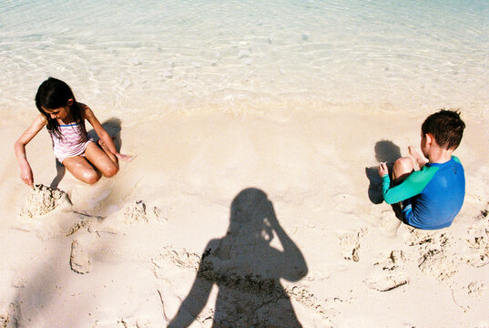 Mother watches two kids play on beach while on family vacation
