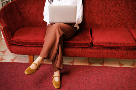 Person using laptop on red vintage sofa