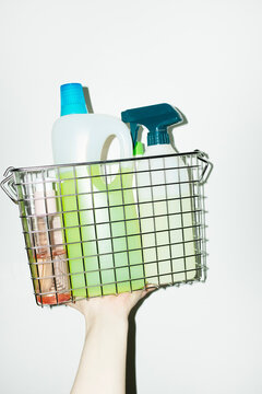 Hand holding wire basket full of cleaning colourful liquid detergents 