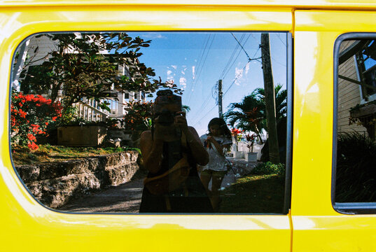 Woman takes selfie with child in the reflection of a car window