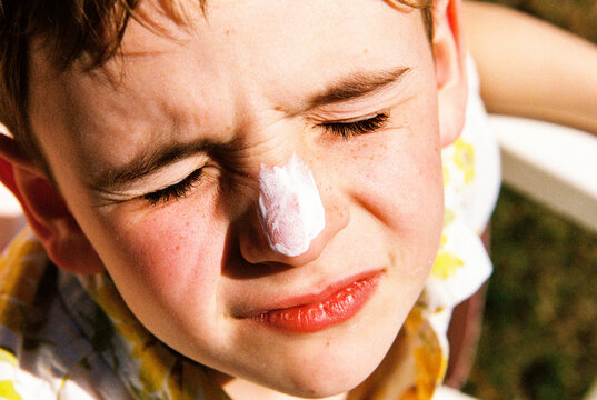 Child squints while getting sunscreen applied to his face