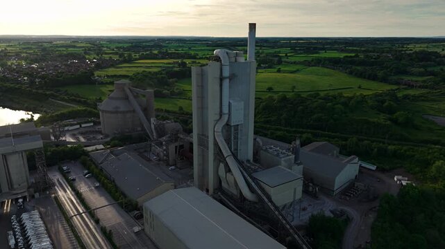Aerial view of the Rugby Cement Plant with its tall towers and industrial structures surrounded by green fields and trees in Rugby, England, United Kingdom.