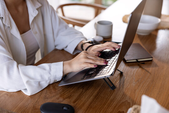 Woman typing on laptop at wooden desk with coffee.