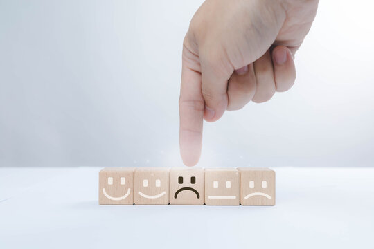 Customer feedback concept with wooden emotion blocks and a hand selecting a negative rating, representing customer dissatisfaction, service quality issues, complaint management, user experience.