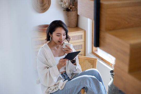 Woman relaxes with coffee and tablet in bright room.