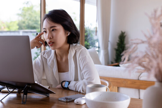 Woman working from home on laptop, thoughtfully engaged.
