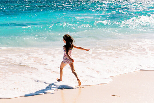 Happy, excited child on tropical vacation runs into turquoise water