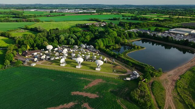 Aerial view of Satellite Mediaport Services with numerous satellite dishes near a pond and green fields in Long Lawford, England, United Kingdom.