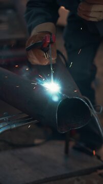 Professional metalworker creates strong welded connection on heavy steel pipe using industrial equipment. Intense blue arc and hot sparks highlight modern manufacturing and skilled labor.