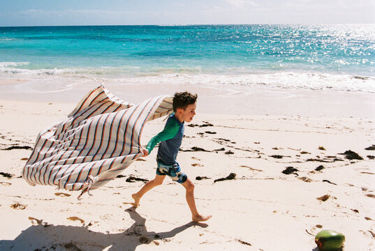 Child running on beach with towel flying behind him