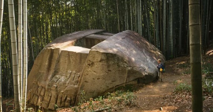 Lone boy touching large stone structure in bamboo grove then walking away - wide, high shot