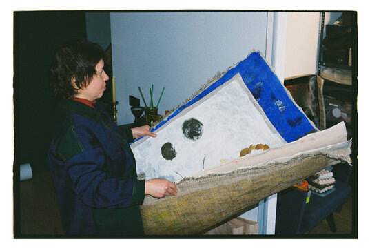 A woman holds a large painting in an art studio.