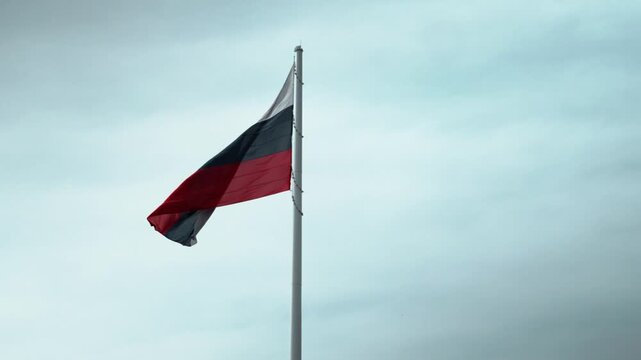 Russian flag flying above official area under moody sky. Image symbolizes government authority, state institutions, diplomacy, leadership and national presence in political or civic context outdoors