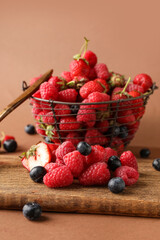Basket with fresh raspberries, blueberries and strawberries on brown background