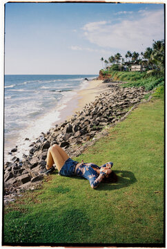 Woman lies on the grass with view of ocean waves 
