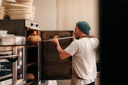 Baker Checks Bread in Gas Deck Oven in Bakery Kitchen