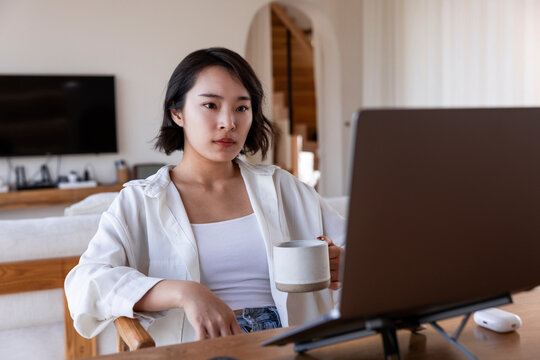 Woman works at laptop with coffee in bright room.