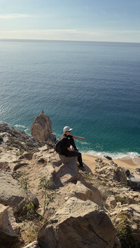 woman sitting on a cliff by high above the ocean on sunny day