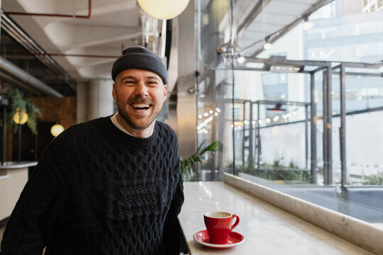 Smiling man wearing beanie having coffee at cafe