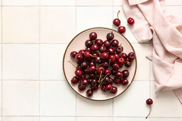Plate with sweet cherries on white tile table