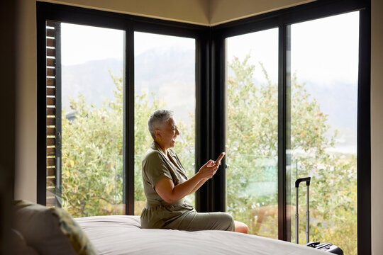 Woman texting by smartphone and laughing at hotel room