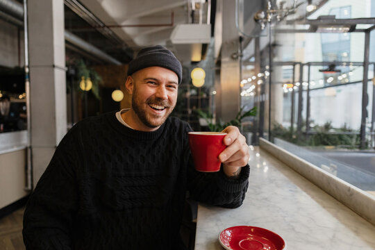 Smiling man enjoying coffee at modern cafe window