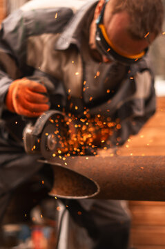 Construction specialist cuts damaged steel pipeline with angle grinder during repair operation outdoors. Bright sparks, industrial tools illustrate infrastructure maintenance and engineering service