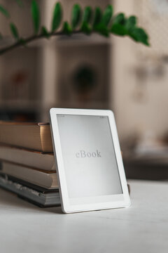Minimalist home workspace with ebook reader and books stack. Concept of focused work, remote productivity and balanced lifestyle with technology and natural elements.
