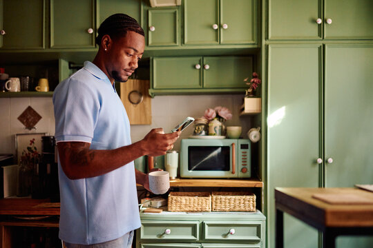 Young Black Man Checking Smartphone During Break in Kitchen
