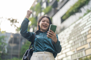 Fototapeta premium Asian happy businesswoman reading great news on smartphone and raising fist celebrating success, Concept of corporate victory, financial wealth, goal achievement and modern professional lifestyle