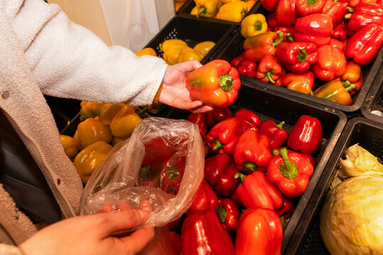 Person Picking Red Bell Peppers into Bag at Grocery Store