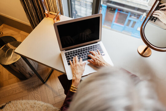 Senior woman using laptop typing on keyboard working remotely