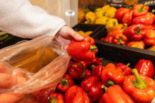 Person Picking Red Bell Peppers into Bag at Grocery Store