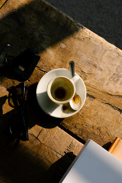 Sunlit detail of empty coffee cup, sunglasses, books, and hotel key