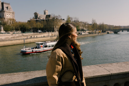 A female tourist admiring the Seine River as a boat passes behind her