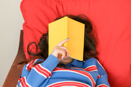 Woman hiding face with yellow book