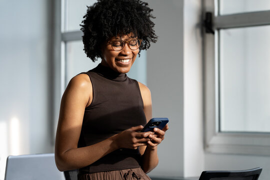Happy black woman messaging on smartphone in office