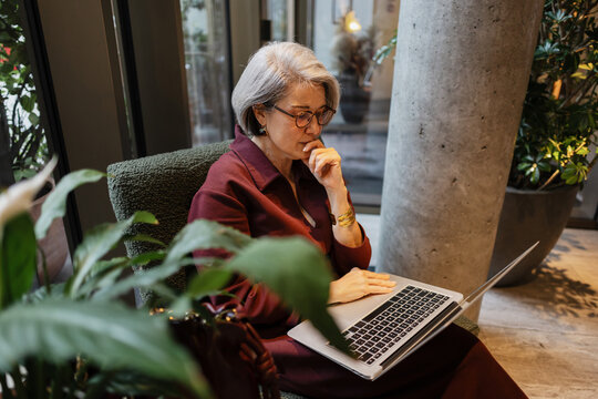 Senior woman working on laptop thinking about business strategy
