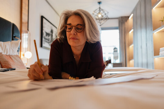 Grey-haired Senior woman writing paperwork on a bed