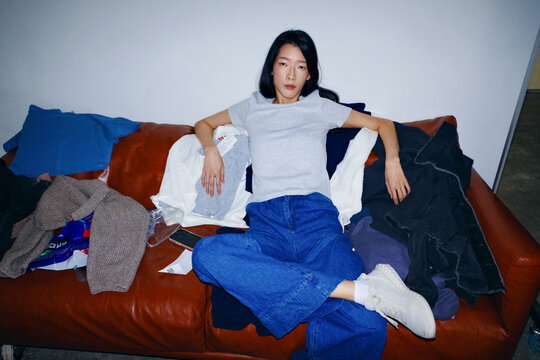 Person relaxing on a couch surrounded by clothes