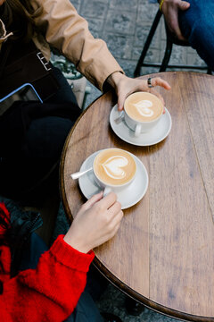 Anonymous people holding two cups of latte decorated with latte art